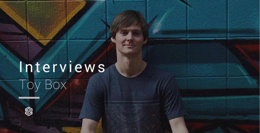 Joe Garston, a young man, stands confidently in front of a graffiti wall adorned with the words "interviews" and "toy box.