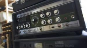 A man is standing in front of a stack of guitar amps, surrounded by the powerful sound of dub drums.