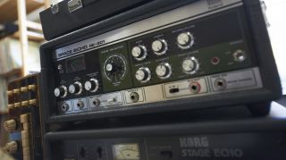 A man is standing in front of a stack of guitar amps, surrounded by the powerful sound of dub drums.