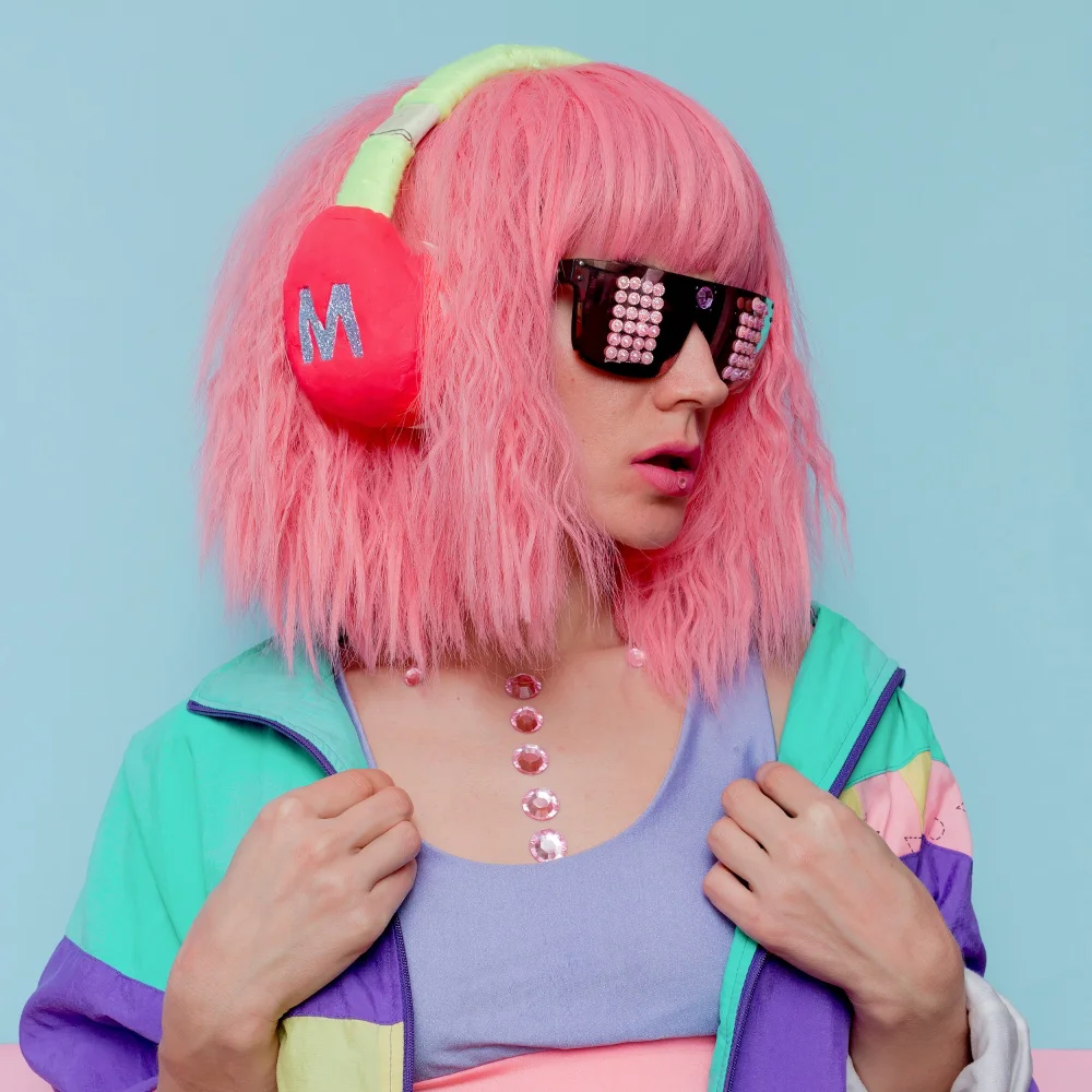 A girl with pink hair wearing headphones and a colorful jacket listens to the Perfect Sound through her Ultimate Guide.