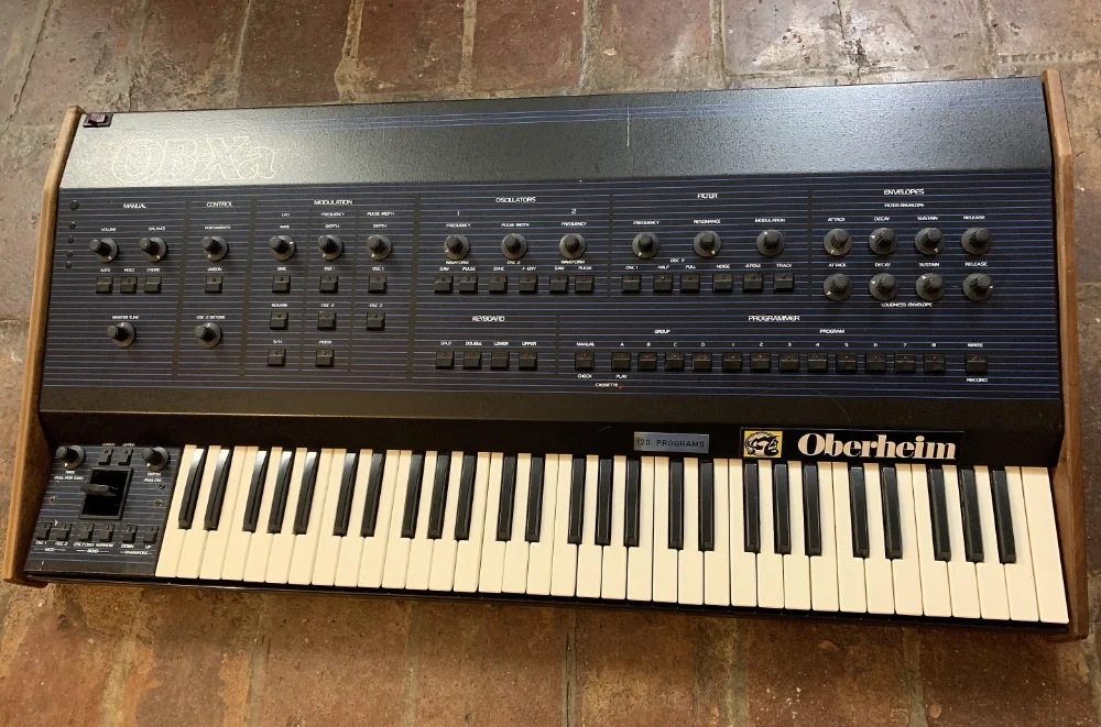 An Oberheim OB-X analog synthesizer sitting on a brick floor.