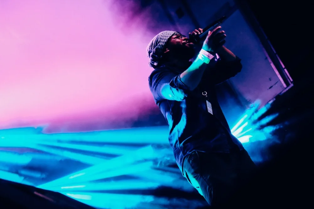 A man on stage with a microphone in front of a purple light, adjusting the sound.