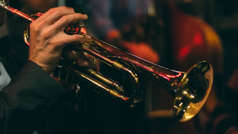 A man in a suit playing a trumpet, showcasing his mastery of the instrument.